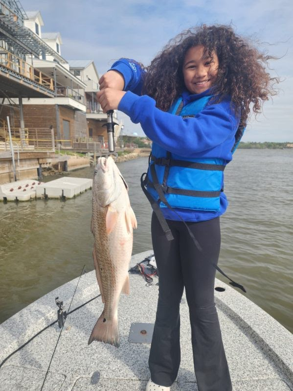 Young angler in a blue life jacket holding a redfish at the dock