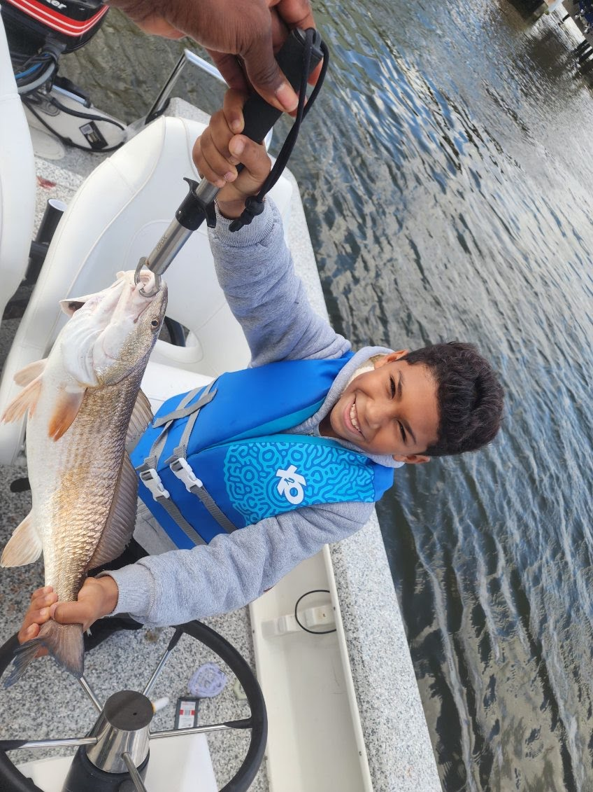 Young angler in a blue life jacket holding a redfish